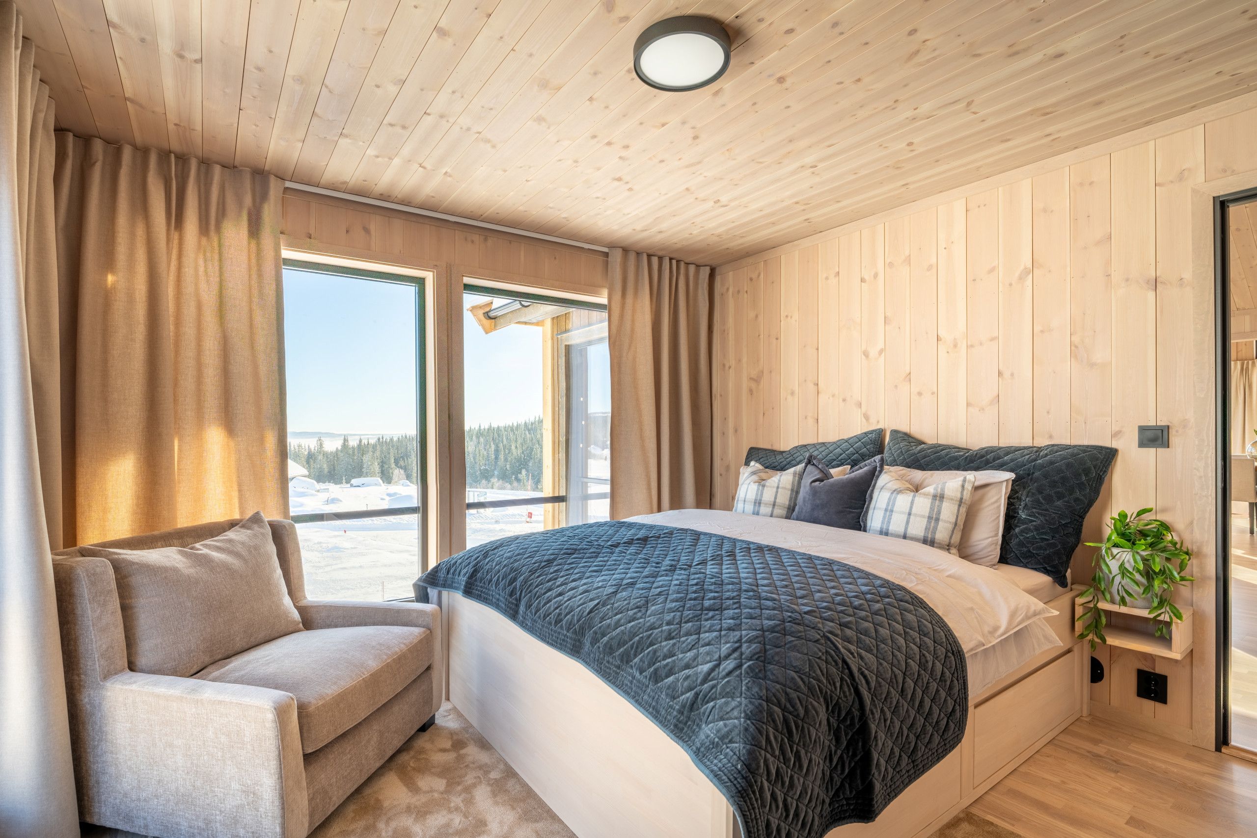 Une chambre à coucher avec un grand lit, une chaise, une fenêtre avec des rideaux et une vue sur un paysage enneigé.