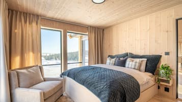 Une chambre à coucher avec un grand lit, une chaise, une fenêtre avec des rideaux et une vue sur un paysage enneigé.