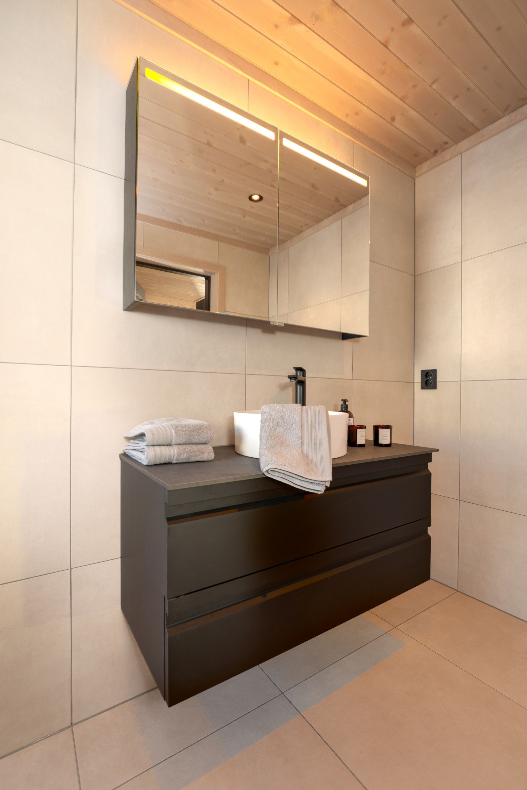 A modern bathroom with a large mirror, dark vanity, and neatly folded towels.