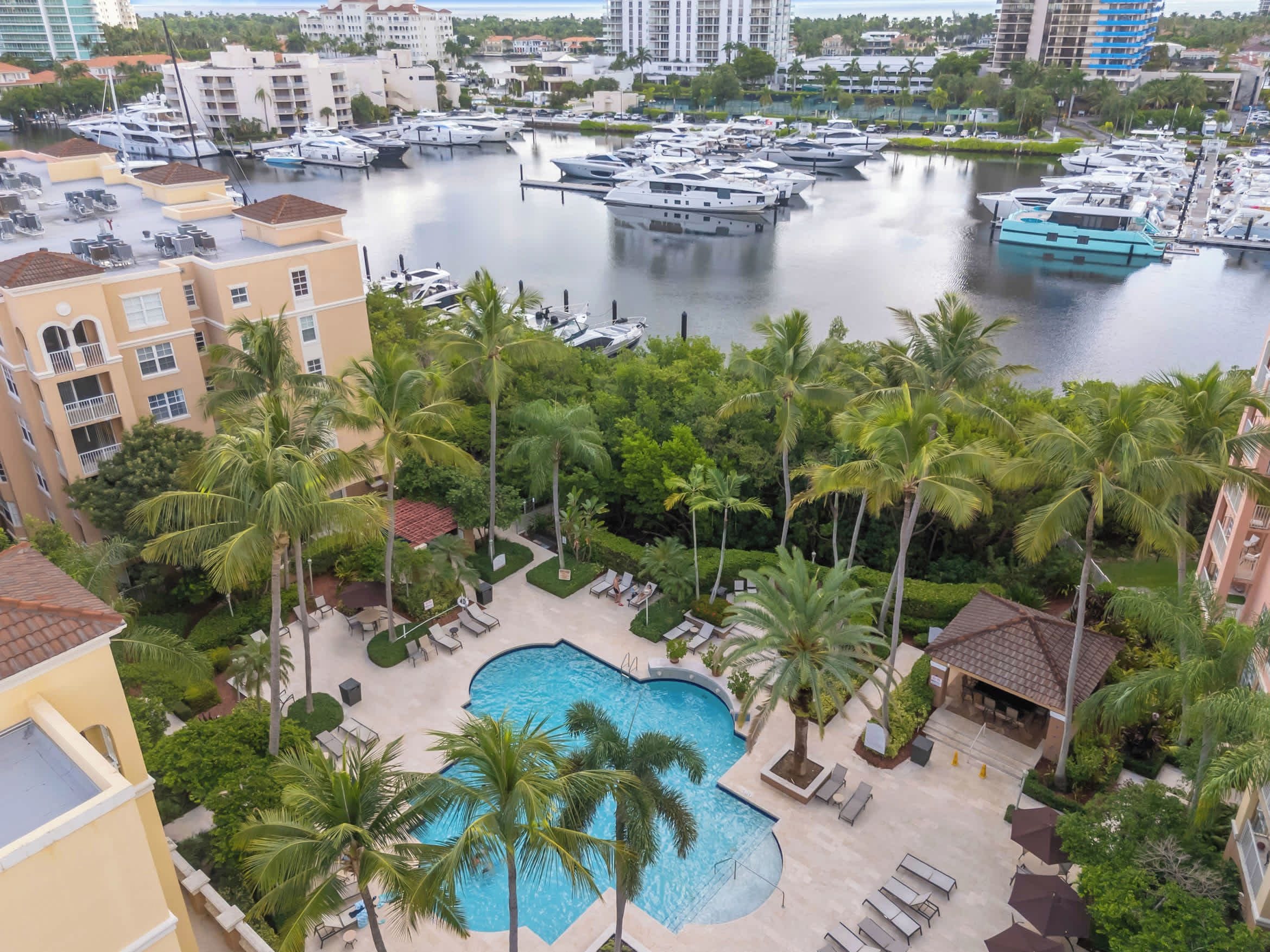 A marina with boats, a swimming pool surrounded by palm trees, and residential buildings.