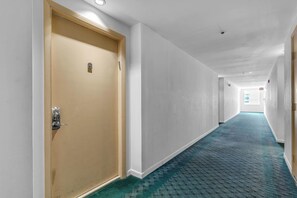 Ein Hotelgang mit Teppichboden, einer Tür mit Schloss und einer Leuchte an der Decke.