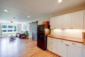 A spacious kitchen with wooden flooring, white cabinets, and a black refrigerator.