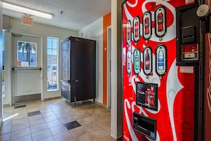A vending machine with various drink options, a push-to-exit door, and a view of the outside. - Motel 6 Tucson, Az - North_1 King Bed | (Tucson)