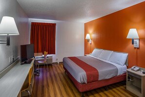 A hotel room with a bed, bedside tables, a desk with a chair, a television, and a window with curtains. - Motel 6 Tucson, Az - North_1 King Bed | (Tucson)