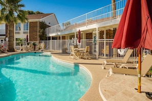 A swimming pool with lounge chairs and umbrellas, a covered patio area, and a two-story building with a balcony. - Motel 6 Tucson, Az - North_1 King Bed | (Tucson)