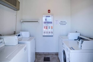 A laundry room with two washing machines, a dryer, and a wall-mounted heater. There is a sign about soap and bleach softeners. - Motel 6 Tucson, Az - North_1 King Bed | (Tucson)