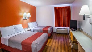 Una habitación de hotel con dos camas, un escritorio, una televisión y una ventana con cortinas.