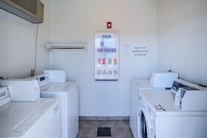 A laundry room with two washing machines, a dryer, and a wall-mounted soap and bleach dispenser. - Motel 6 Tucson, Az - North_2 Queen Beds (Tucson)
