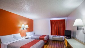 Habitación de hotel con dos camas, un escritorio, un televisor y una ventana con cortinas rojas.
