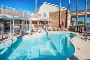 A swimming pool with a clear blue water, surrounded by lounge chairs and umbrellas, with a building in the background. - Motel 6 Tucson, Az - North_2 Queen Beds (Tucson)