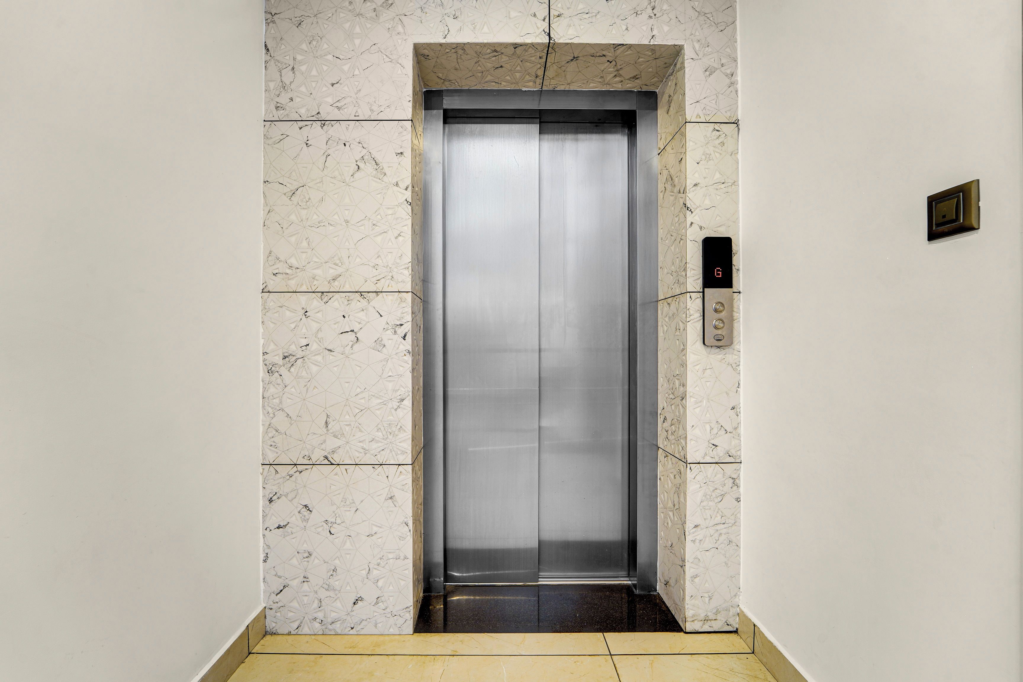 An elevator with a metallic finish, a geometric patterned wall, and a floor with a yellowish tile.