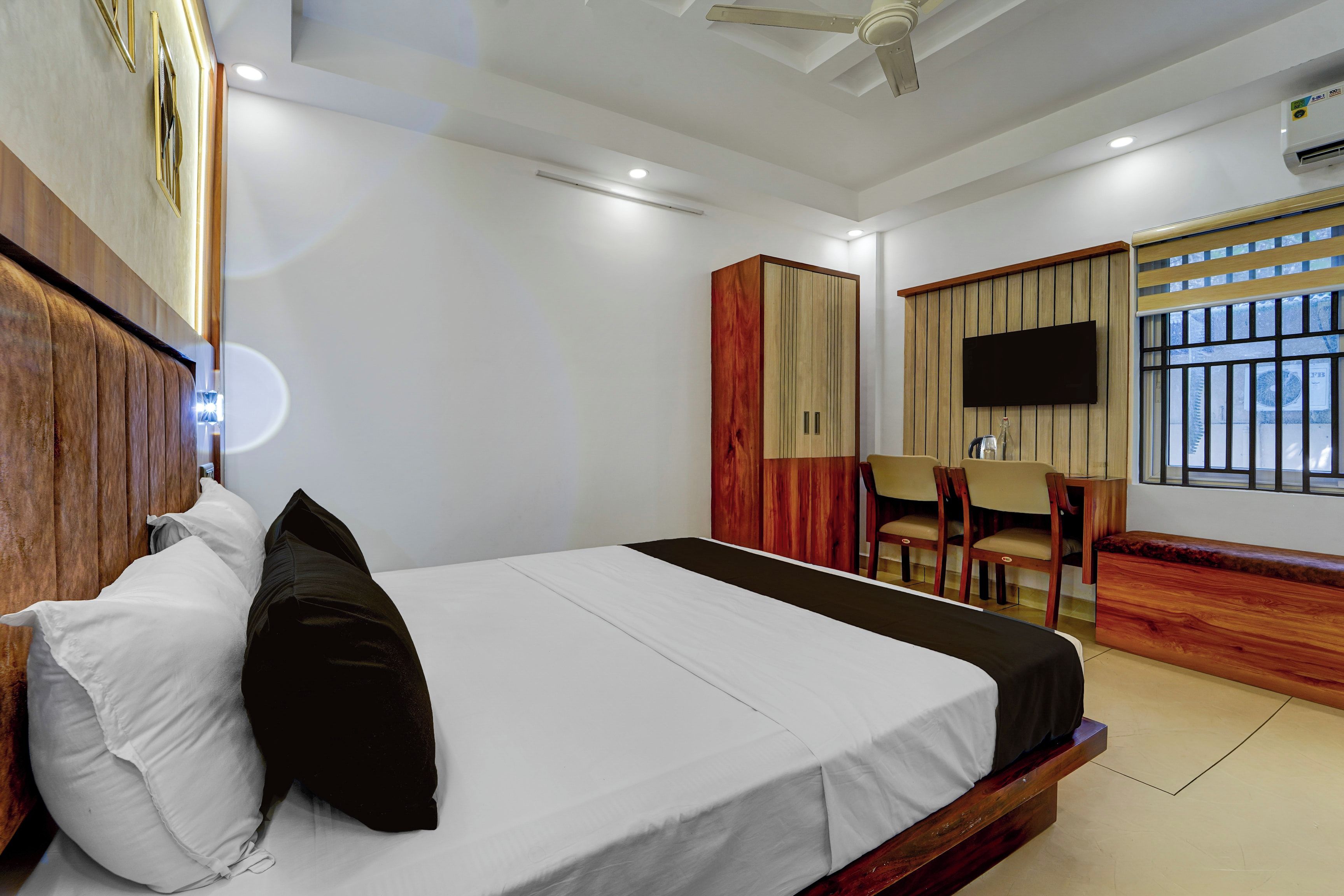 Habitación de hotel con cama, escritorio, silla, televisor y ventana con barrotes.