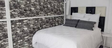 Un dormitorio con pared de piedra, una cama con ropa de cama blanca y una mesita de noche pequeña.