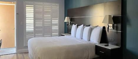 Un dormitorio con una cama grande, una mesita de noche, una lámpara de pared y una puerta con persianas.