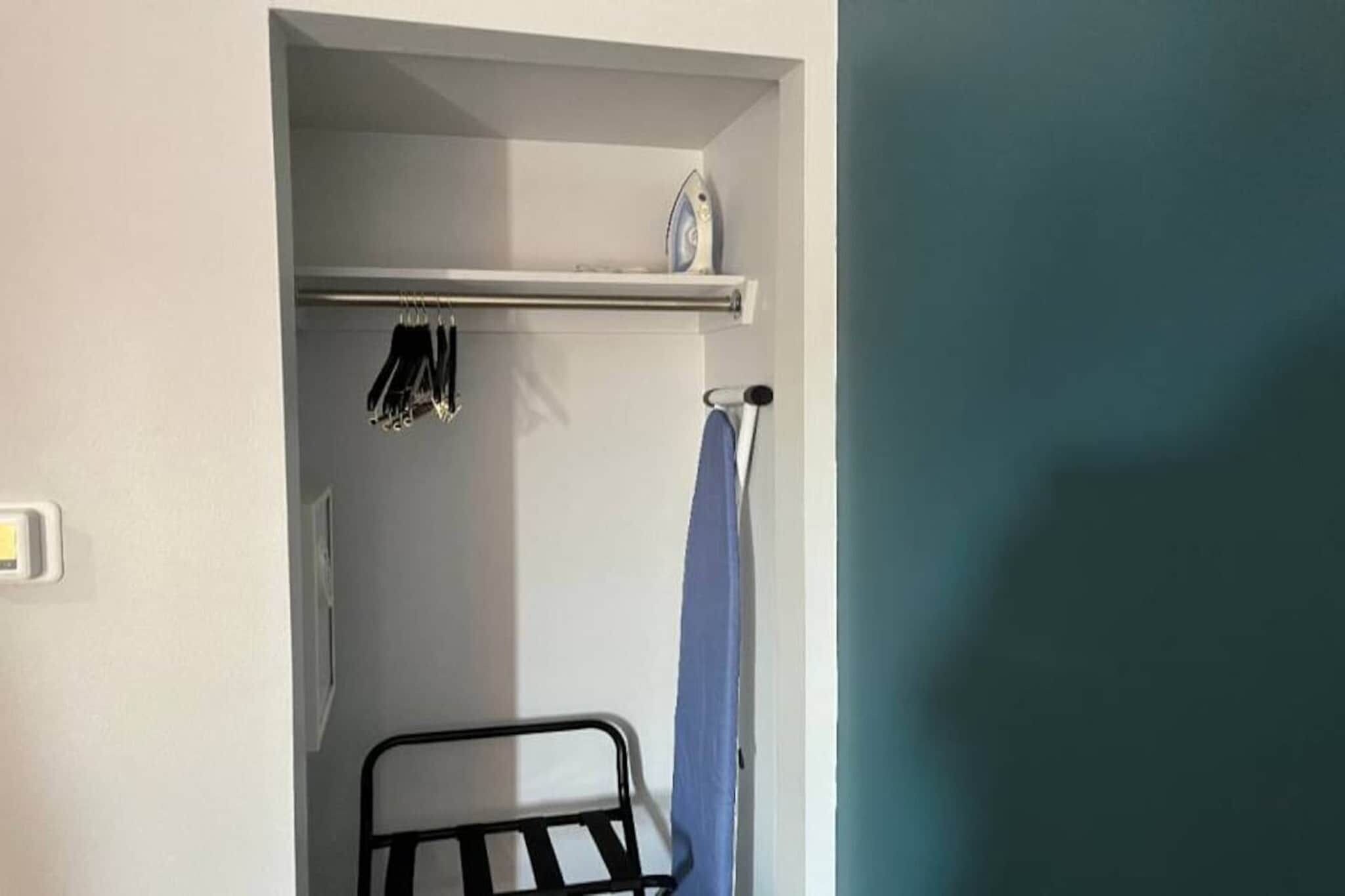 A small room with a metal rack holding hanging items, a towel rack, and a door leading to another room.