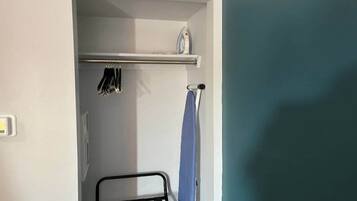 A small room with a metal rack holding hanging items, a towel rack, and a door leading to another room.