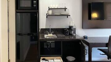 Una kitchenette compacta con microondas, un lavamanos y una cafetera.