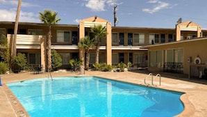 Et hotel med swimmingpool, palmer og en bygning med mange etager og balkoner.