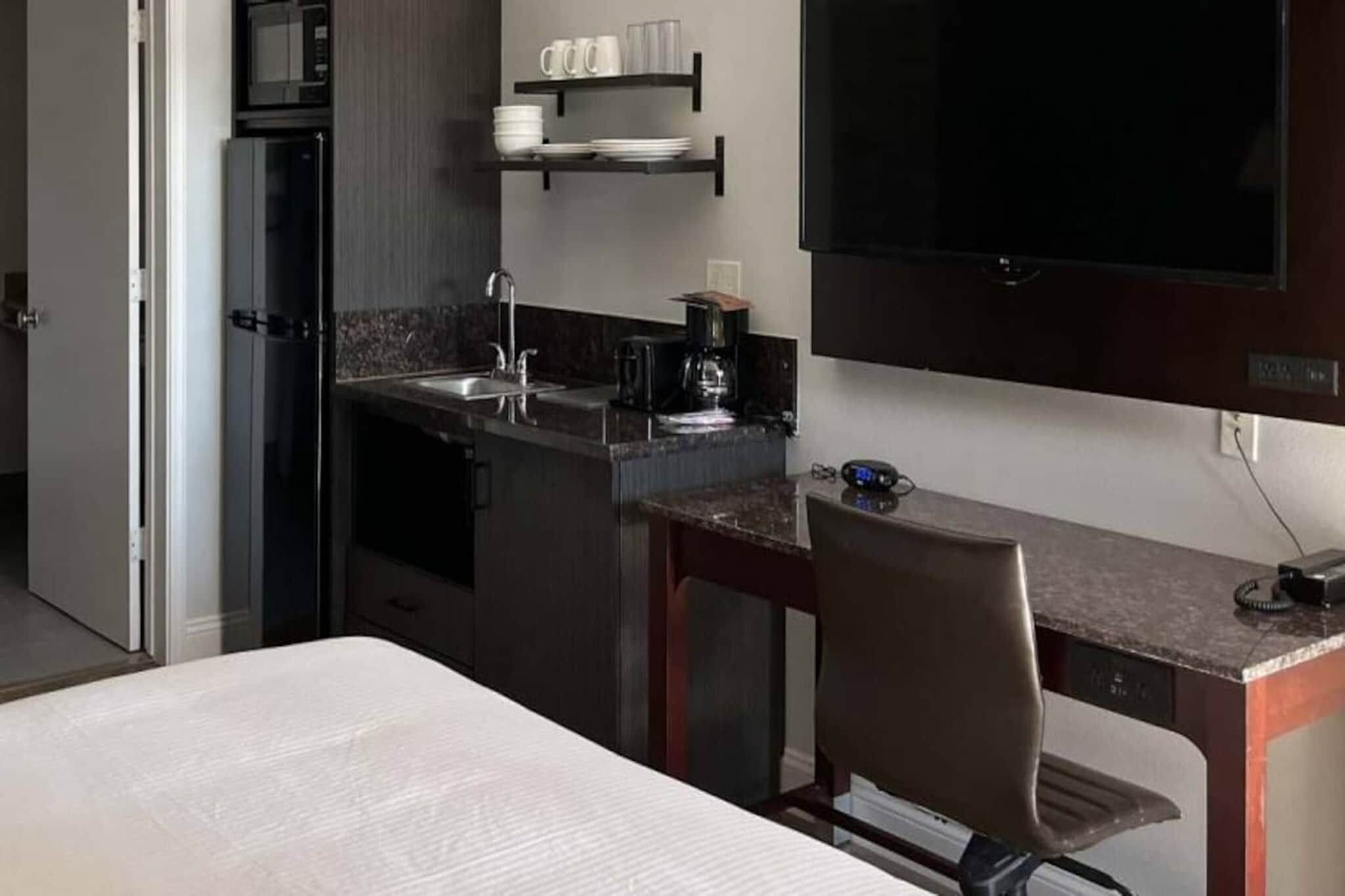 Habitación de hotel compacta con kitchenette, una cama, un escritorio y un televisor.