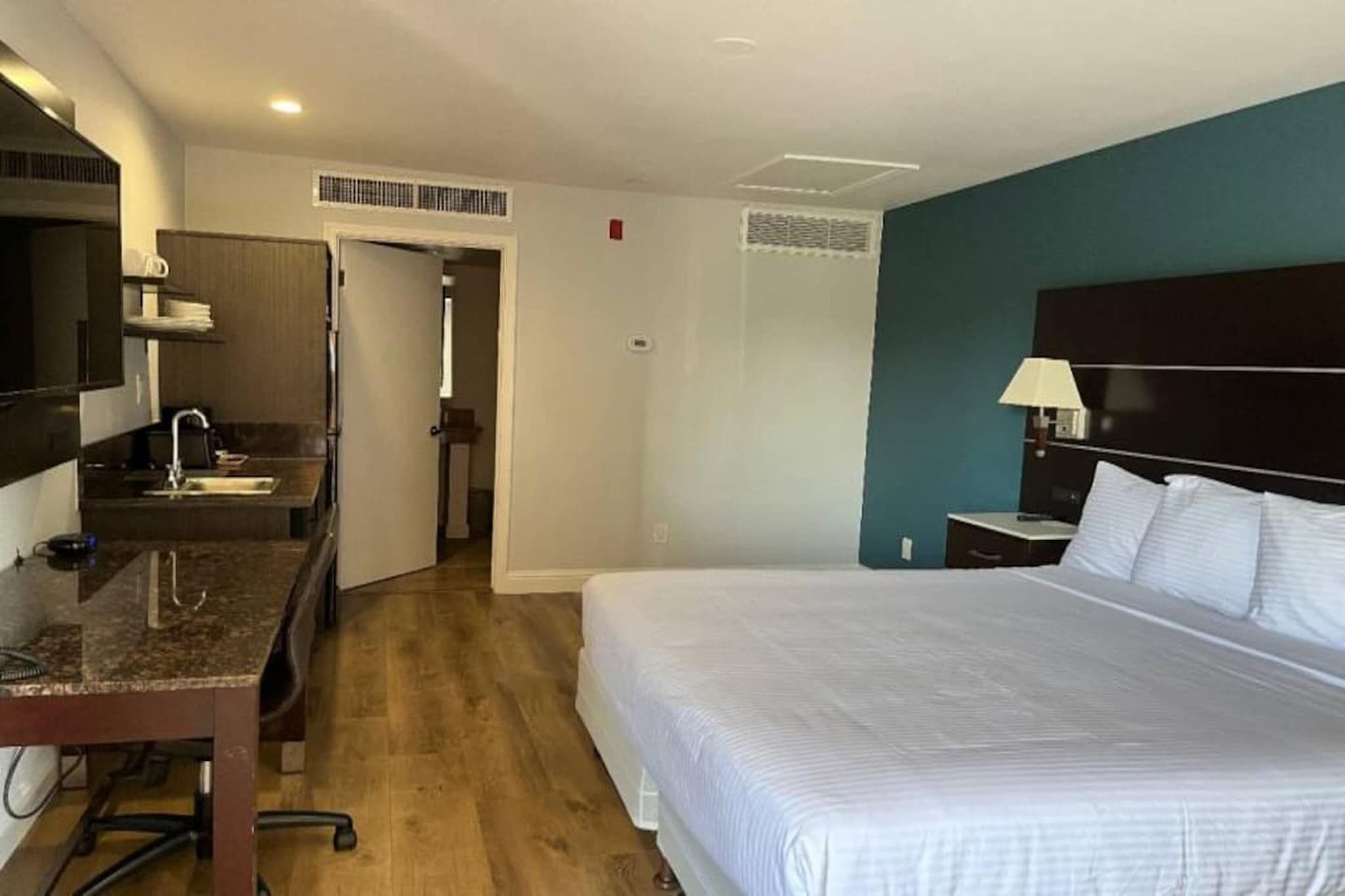 Quarto de hotel com cama, escrivaninha, cadeira, televisão e banheiro.