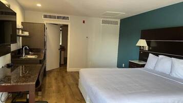 Quarto de hotel com cama, escrivaninha, cadeira, televisão e banheiro.