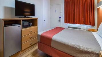 Habitación de hotel con una cama, televisor, microondas y un refrigerador pequeño.