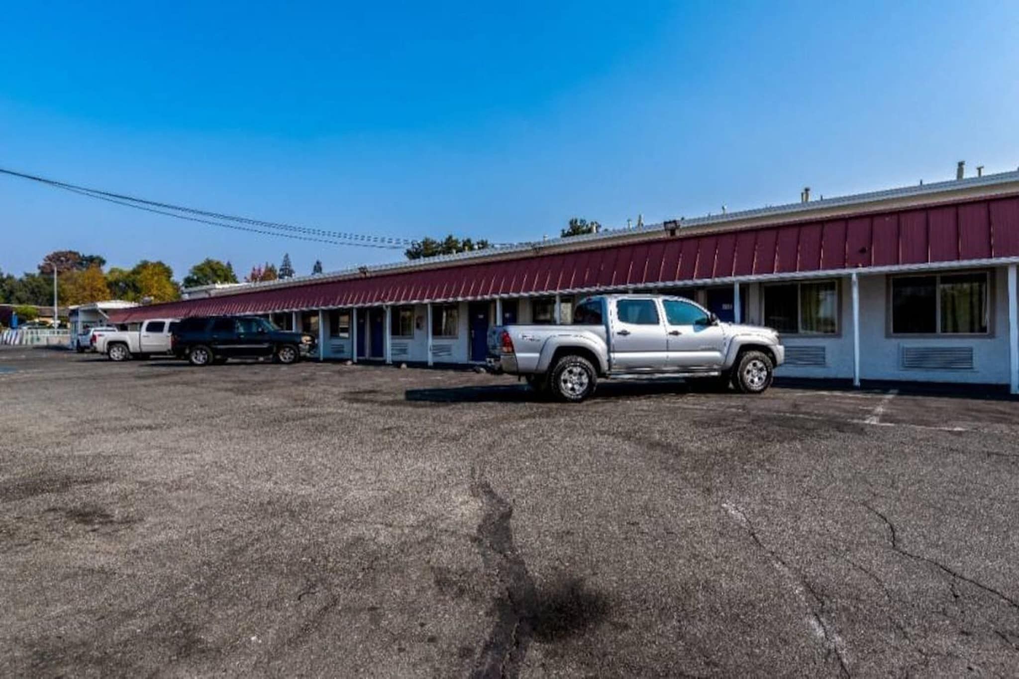 A motel with a row of rooms, a parking lot, and a building with a red awning.