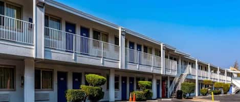 Un motel con varias habitaciones, un estacionamiento techado y una escalera que conduce a un nivel superior.