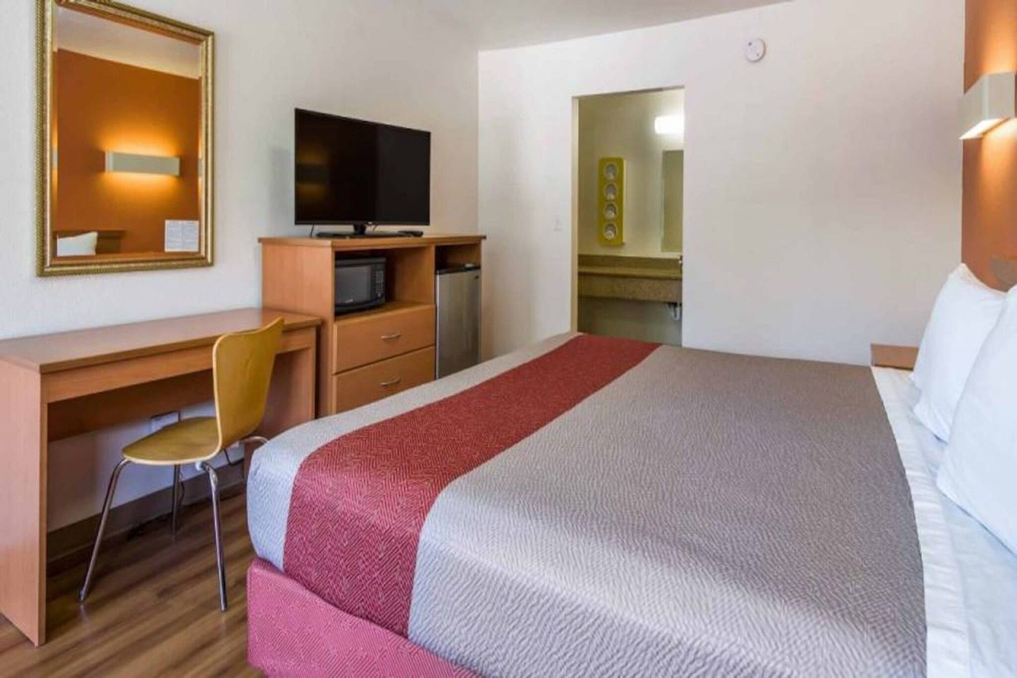 A hotel room with a bed, a desk with a chair, a television, a microwave, and a small refrigerator.