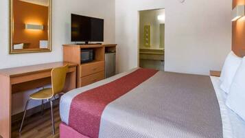 A hotel room with a bed, a desk with a chair, a television, a microwave, and a small refrigerator.