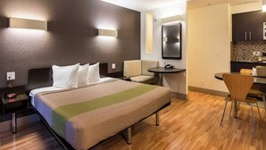 A hotel room with a bed, bedside table, chair, desk, and kitchenette. - Premium King Bed|Pool|Free Parking (Concord)