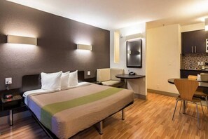 Ein Hotelzimmer mit Bett, Nachttisch, Stuhl, Schreibtisch und Kochnische.