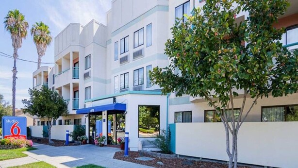 A multi-story hotel with a blue awning, a sign for 'Studio 6', and a well-maintained lawn. - Premium King Bed|Pool|Free Parking (Concord)