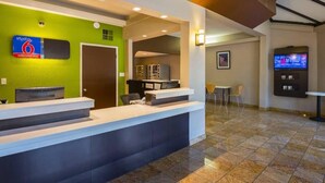 A hotel reception area with a green wall, a reception desk, a TV screen, and a seating area with chairs. - Premium King Bed|Pool|Free Parking (Concord)