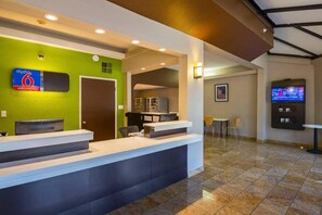 Zona de recepció d'un hotel amb una paret verda, un taulell de recepció, una pantalla de televisió i una zona d'estar amb cadires.