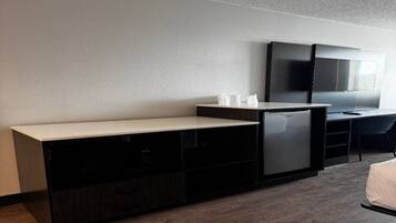 A hotel room with a bed, a desk, a television, and a minibar.