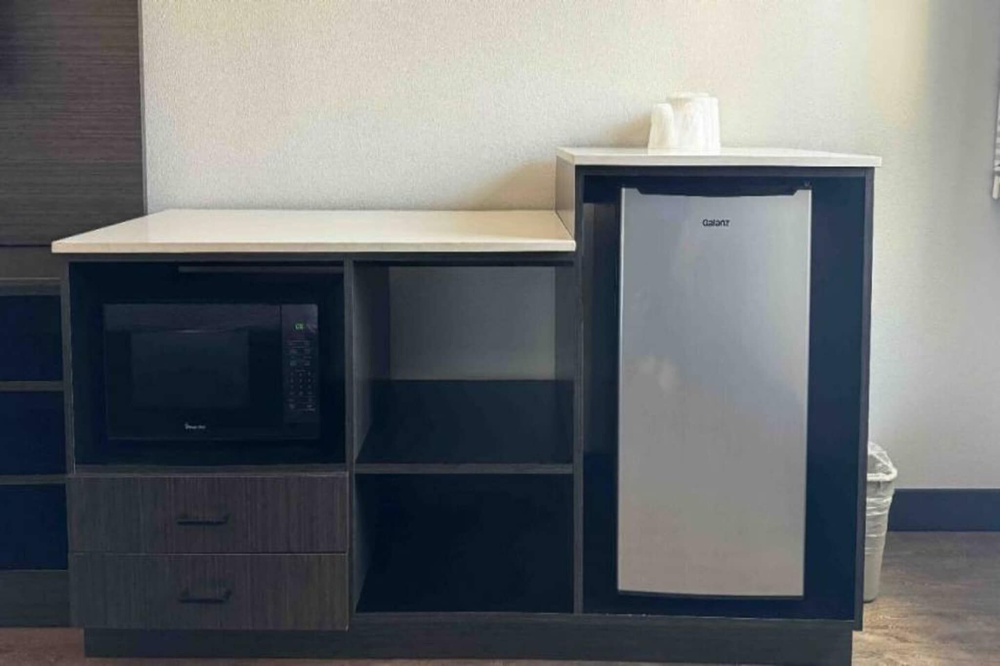 Un angolo cottura con un forno a microonde, un piccolo frigorifero e un piano di lavoro.