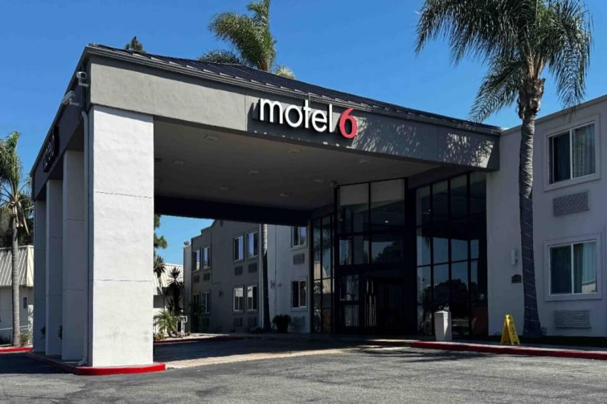 A motel with a covered entrance, palm trees, and a clear sky.