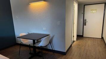 Una habitación con una mesa, dos sillas, una puerta y una lámpara en la pared.