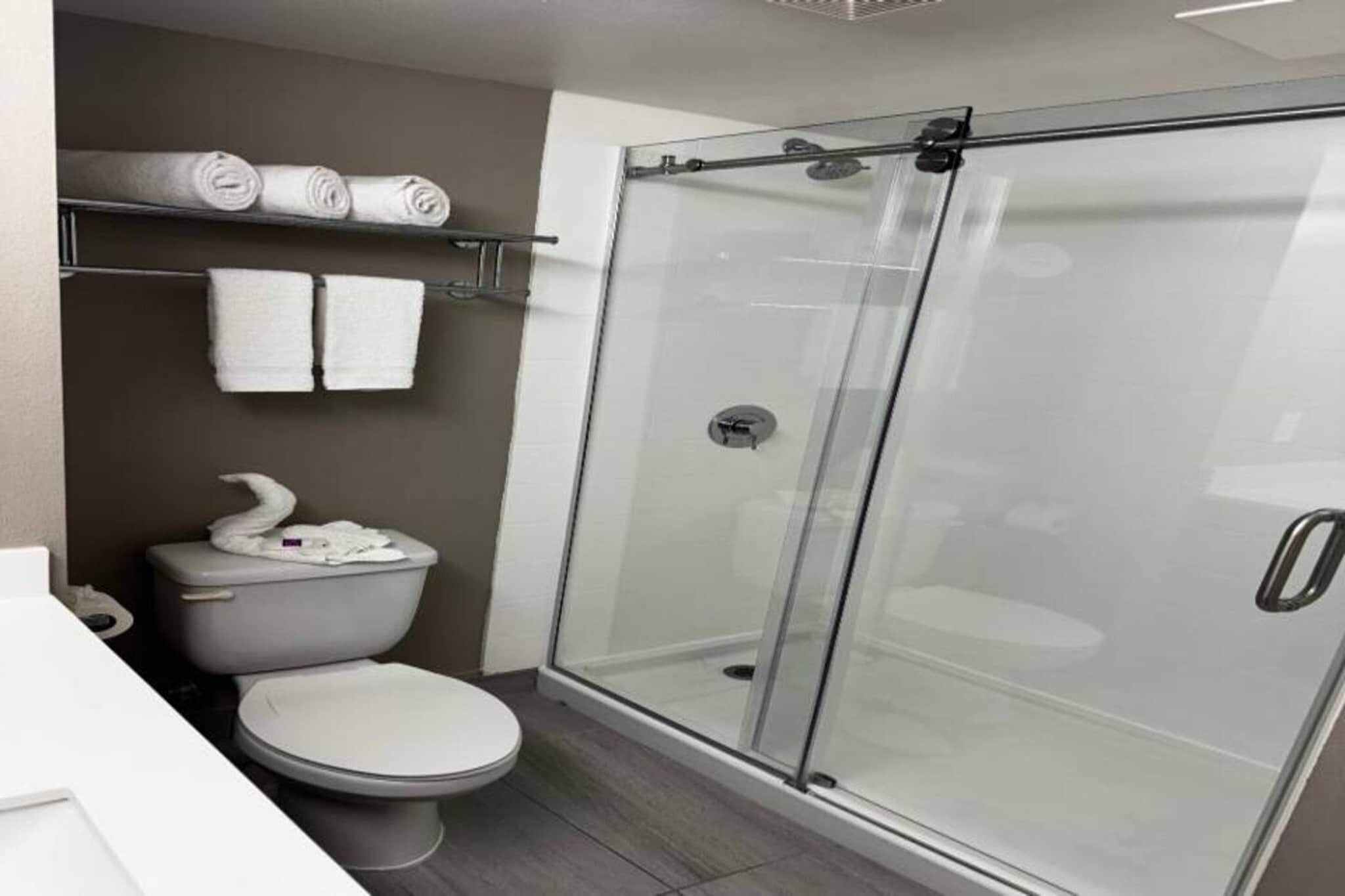 A modern bathroom with a toilet, a glass-enclosed shower, and a towel rack with folded towels.