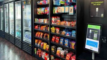 Un'area di self-checkout con un terminale di pagamento digitale e una selezione di snack e bevande sugli scaffali.