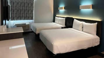 A hotel room with two beds, a desk, and a window with patterned curtains.