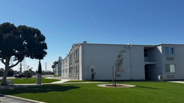 Un edificio moderno con tetto piatto, un piccolo albero al centro e un cielo azzurro limpido.