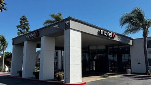 Un motel con area di parcheggio coperta, una insegna con il nome dell'esercizio e una palma sullo sfondo.