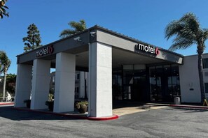 Een motel met een overdekte parkeerplaats, een bord met de naam en een palmboom op de achtergrond.