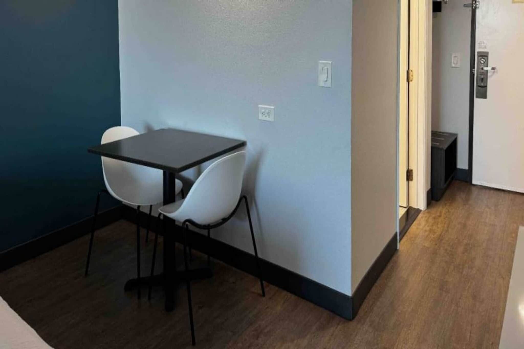 A small room with a table and two chairs, a door, and a light switch on the wall.