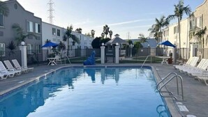 Una piscina con lettini e ombrelloni, circondata da edifici e palme.