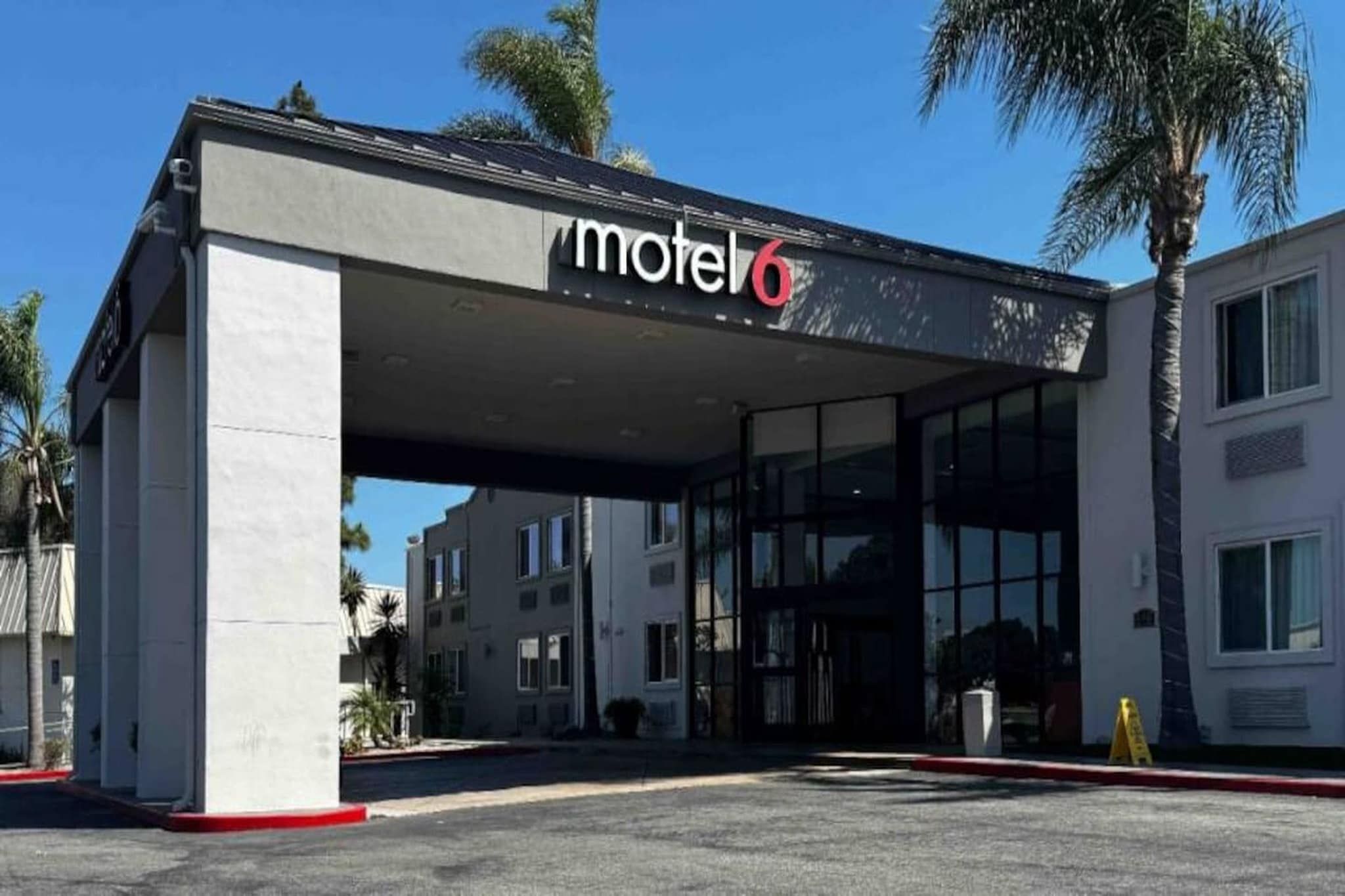 A motel with a covered entrance, palm trees, and a clear sky.