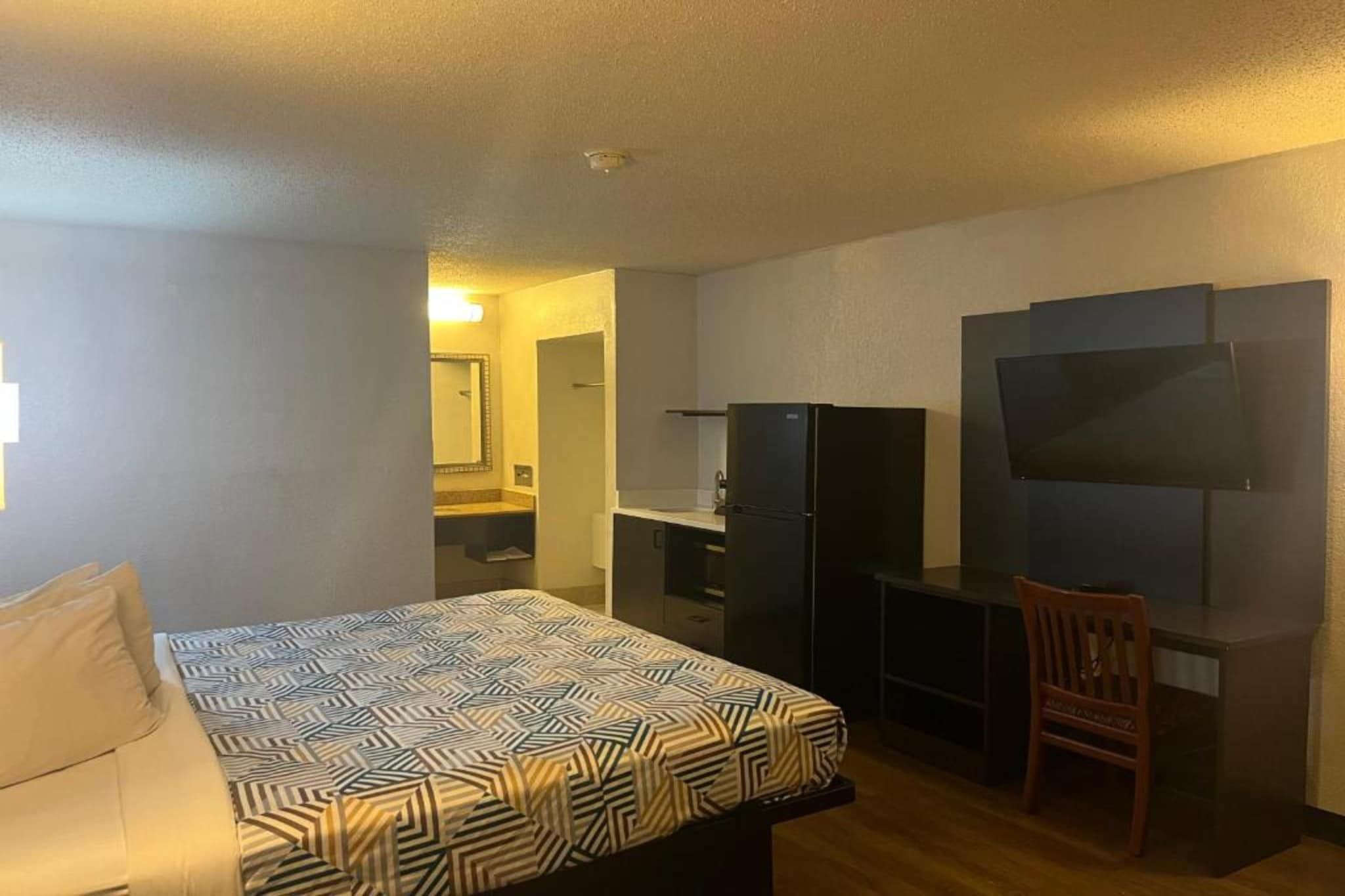 A hotel room with a bed, a desk, a chair, a TV, and a wardrobe.