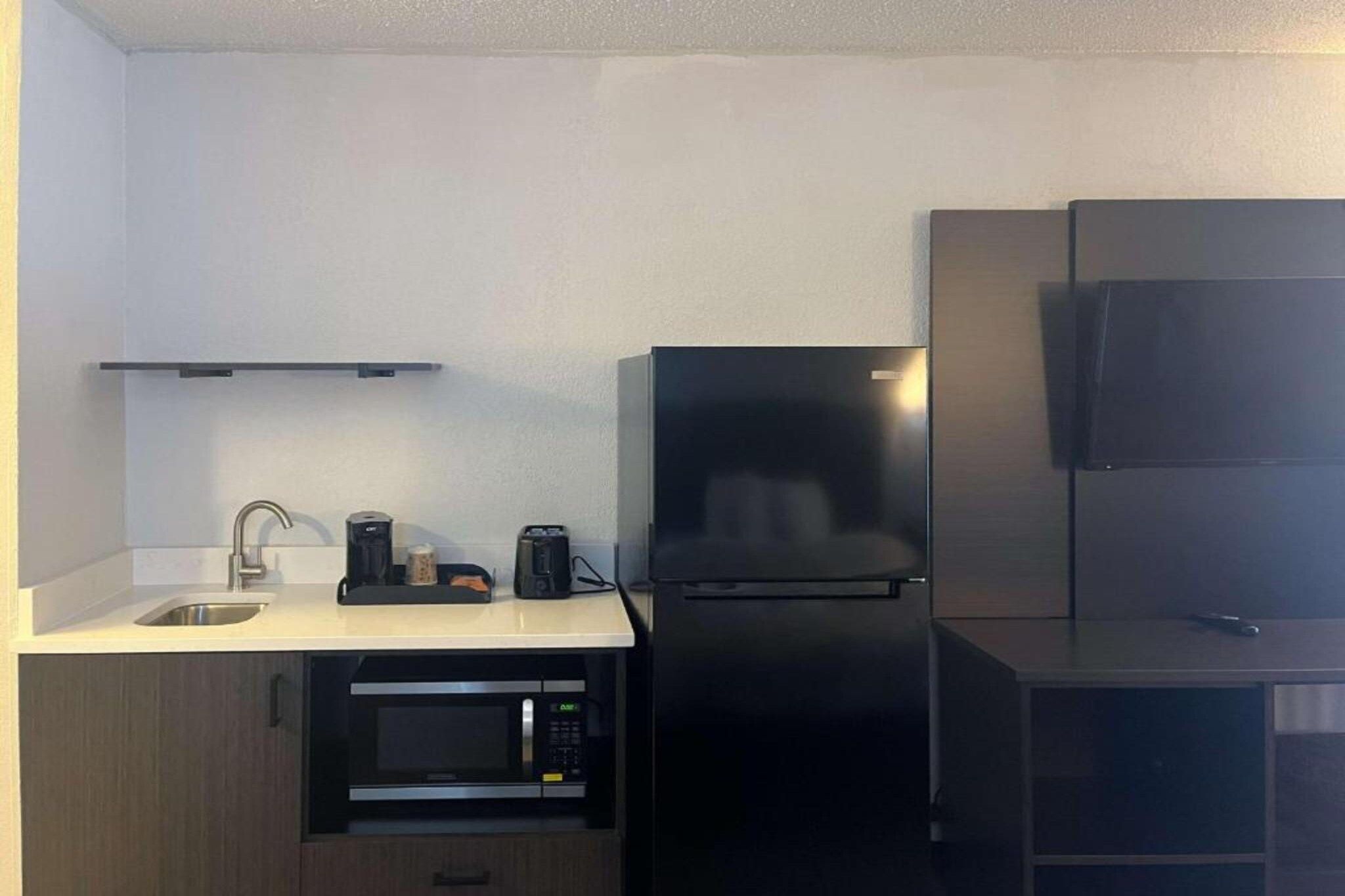 Una cocina compacta equipada con un lavamanos, un microondas, una cafetera y un refrigerador.